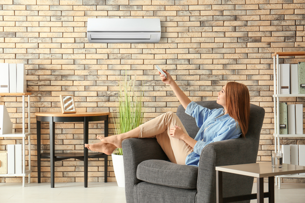 Young,Woman,Switching,On,Air,Conditioner,While,Sitting,In,Armchair